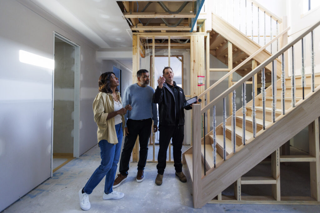 woman and two men standing at the bottom of stairs in a home under construction.